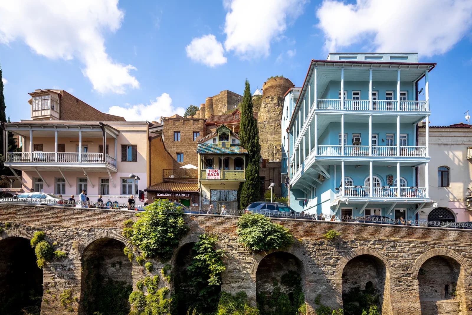 Houses with carved wooden balconies above an arched stone wall in Abanotubani, the old bath district of Tbilisi