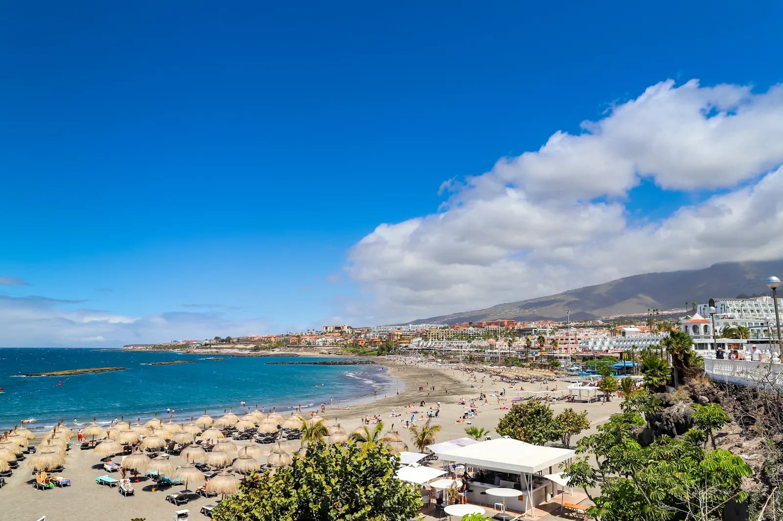 Playa de Torviscas in Costa Adeje seen from above, with straw parasols, the bay and low-rise hotels stretching towards the hills