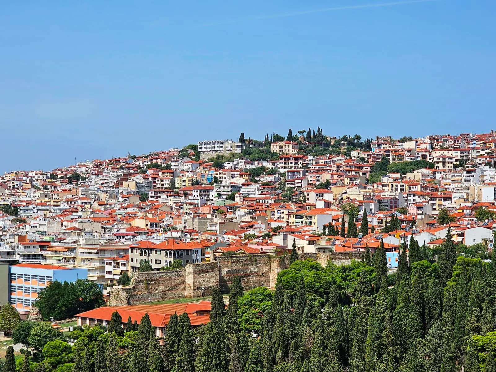 The houses and red roofs of Ano Poli covering the hill above the Byzantine city walls and a band of cypress trees