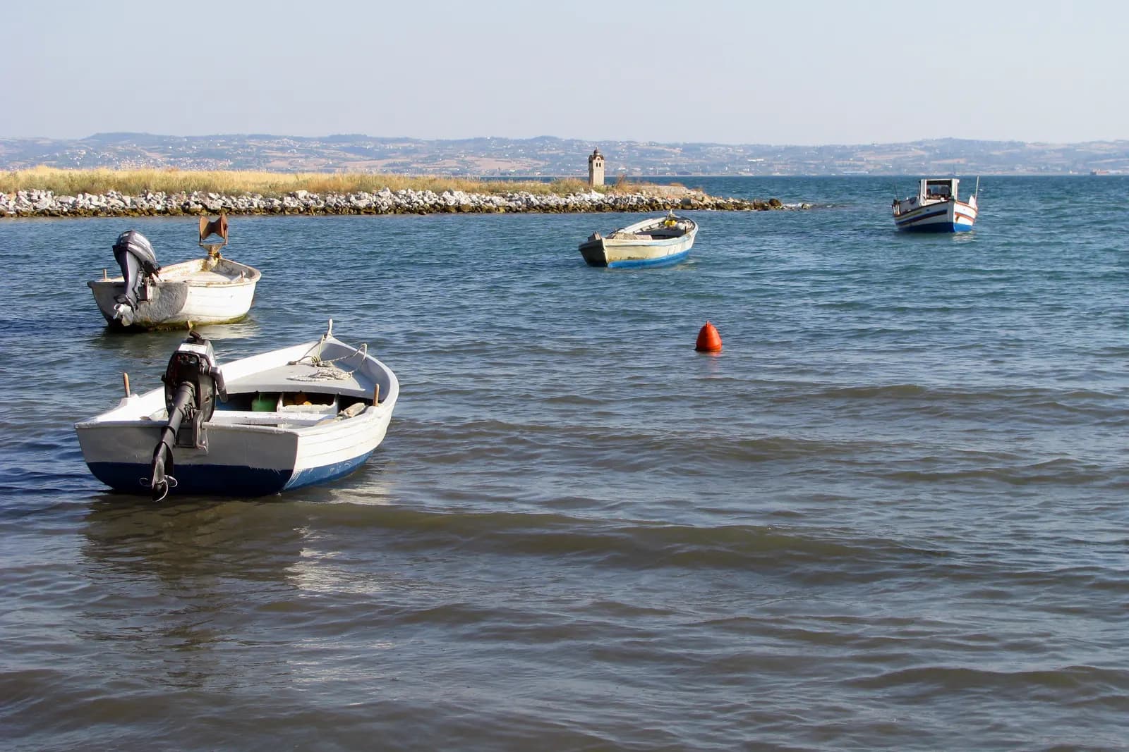 Small fishing boats moored off the shore at Nea Krini in Kalamaria, with a stone breakwater, a small white beacon and the far shore of the Thermaic Gulf behind