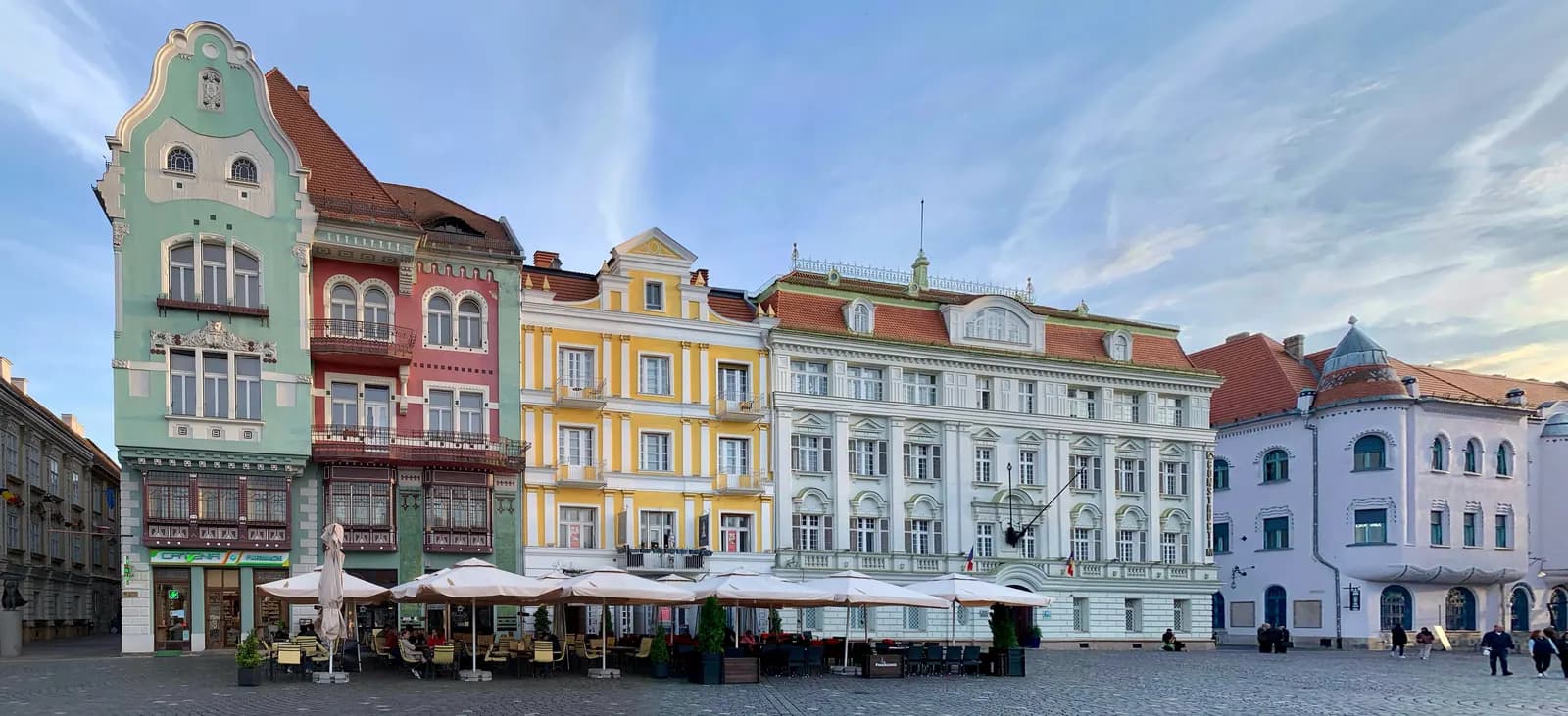 A row of colourful Secession and Baroque houses on Piața Unirii in Timișoara, with café umbrellas on the cobbled square in front
