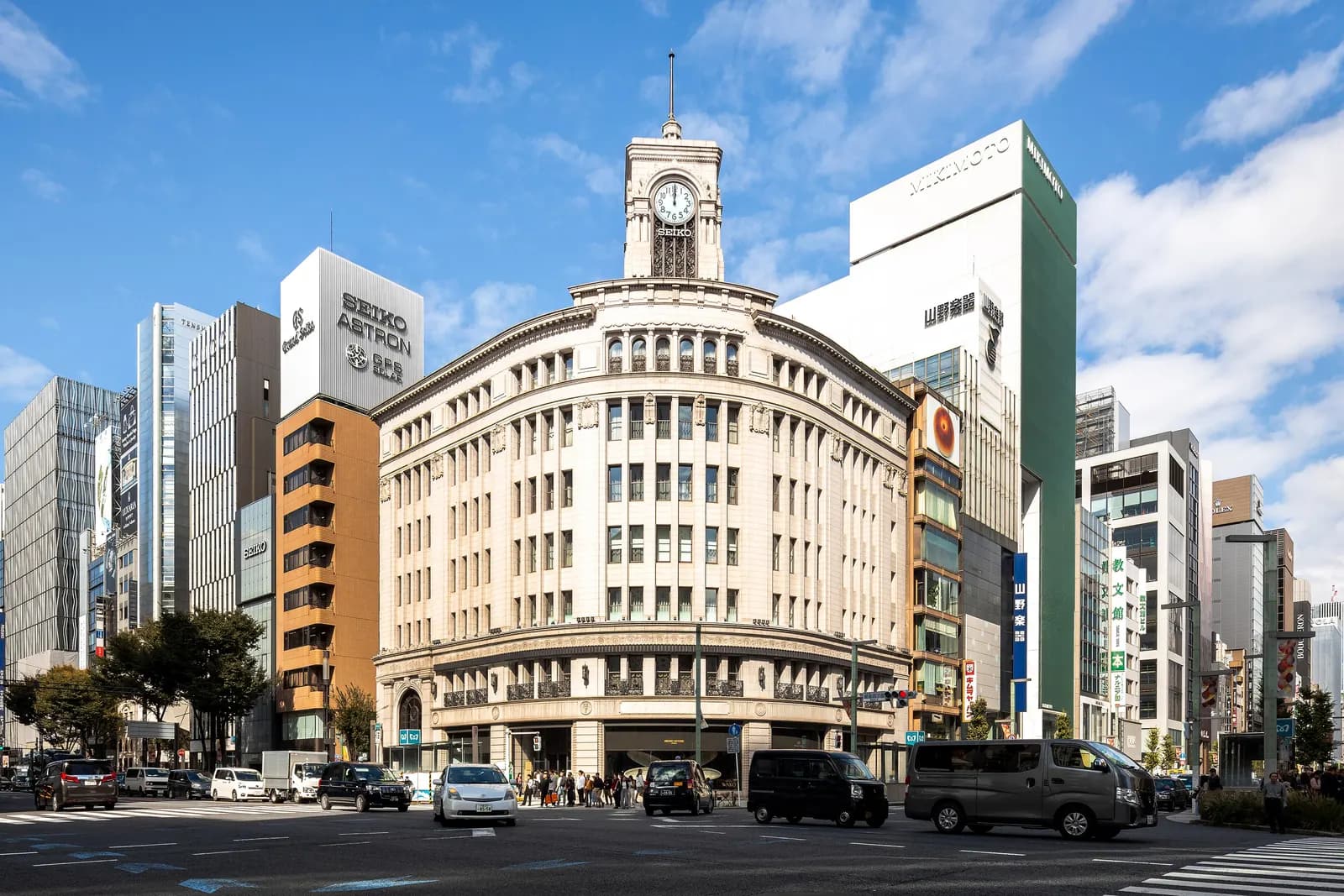 The curved stone Wako building and its clock tower at the Ginza 4-chome crossing, with taxis on the road and shop towers on both sides
