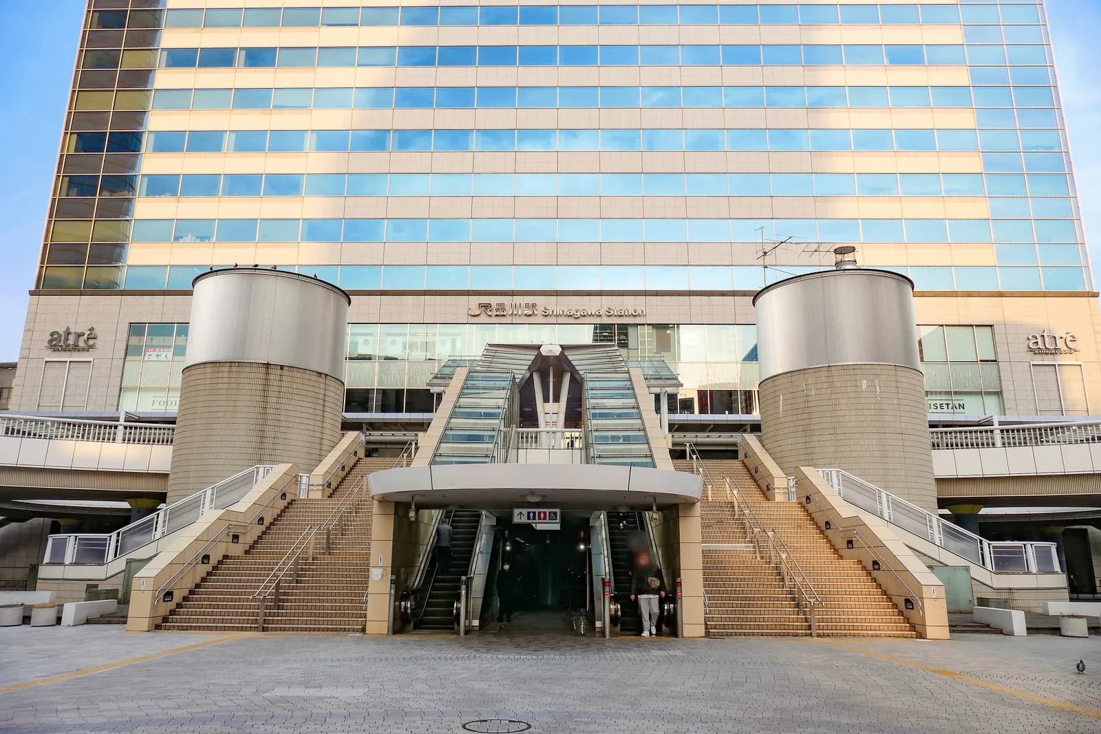 The east (Konan) exit of Shinagawa Station, with twin staircases and escalators below a glass office tower in early morning light