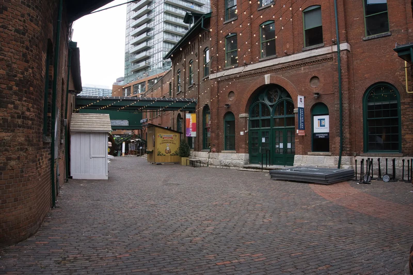 Red-brick former distillery buildings on the brick-paved Gristmill Lane in Toronto's Distillery District, with a residential tower behind