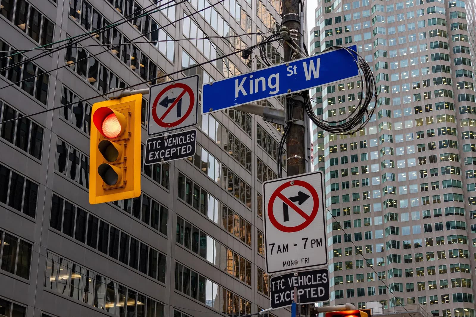 A King St W street sign in Toronto's Financial District with signs banning turns from 7 AM to 7 PM on weekdays, TTC vehicles excepted, in front of office towers