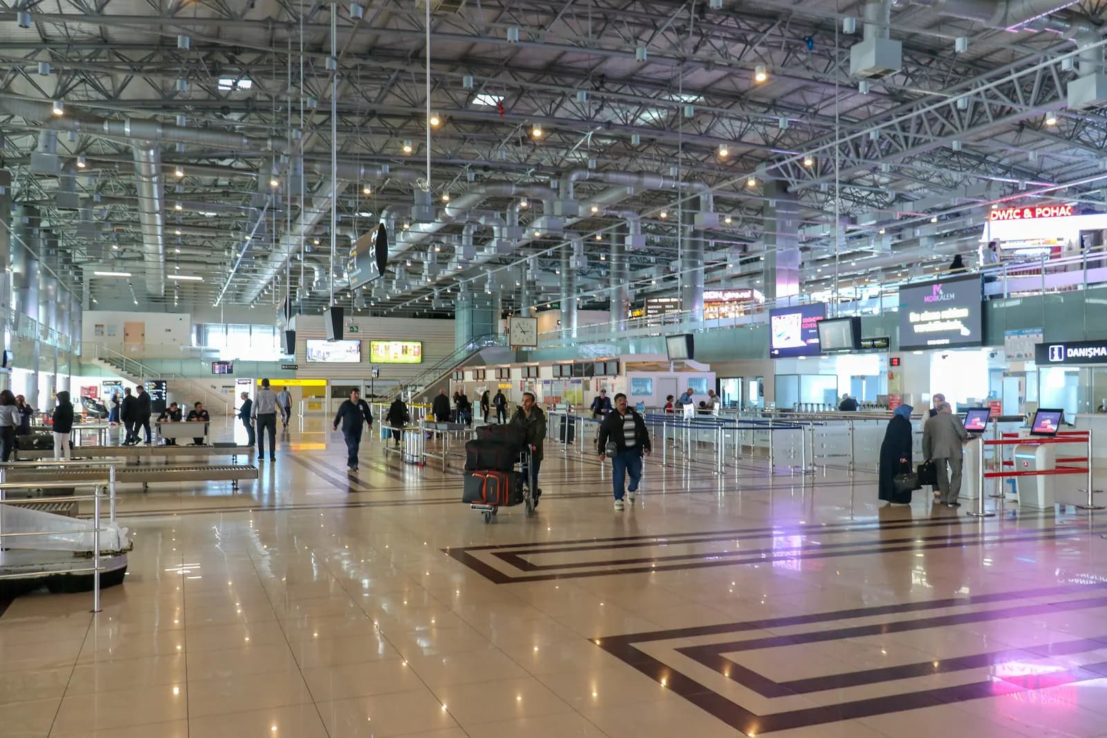 The check-in hall of Trabzon Airport, with travellers and luggage trolleys under a steel roof