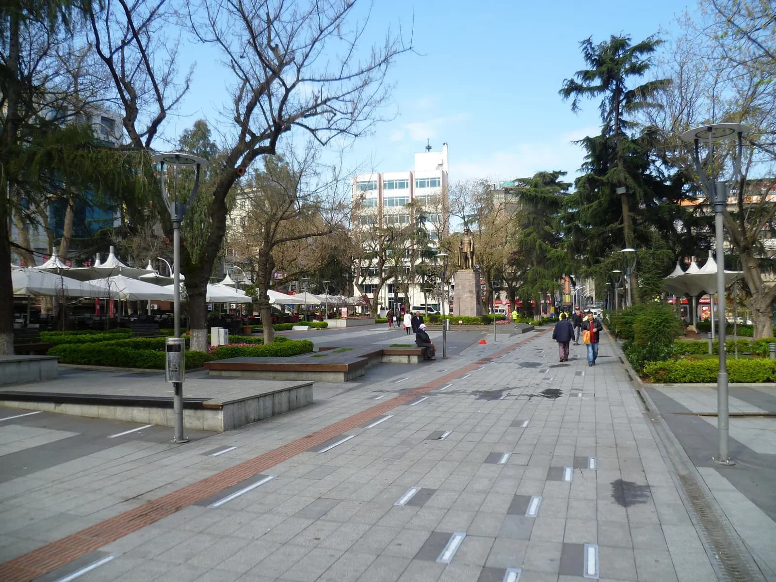 The paved walkway through Meydan Park in central Trabzon, with café umbrellas, trees and a statue on a plinth
