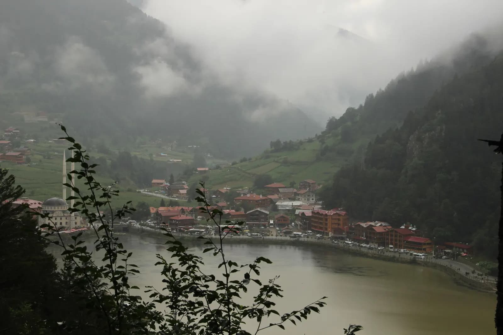 The lake at Uzungöl with the village, a mosque and hotels along the shore, under low cloud on the wooded mountains