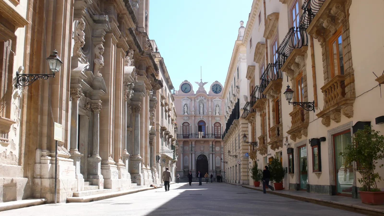 Corso Vittorio Emanuele in the old town of Trapani, a paved street between baroque palace fronts with the twin clocks of Palazzo Senatorio at the far end