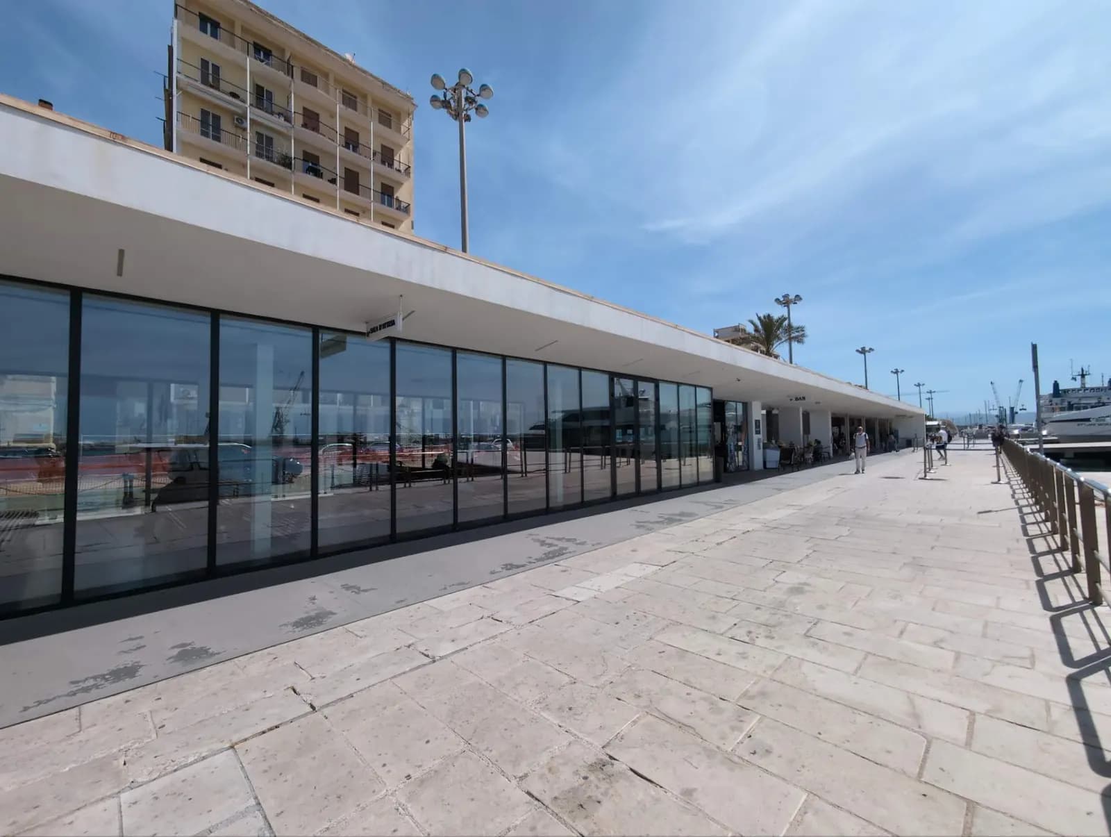 The ferry terminal on the quay at Trapani, a long low glazed building with the harbour behind