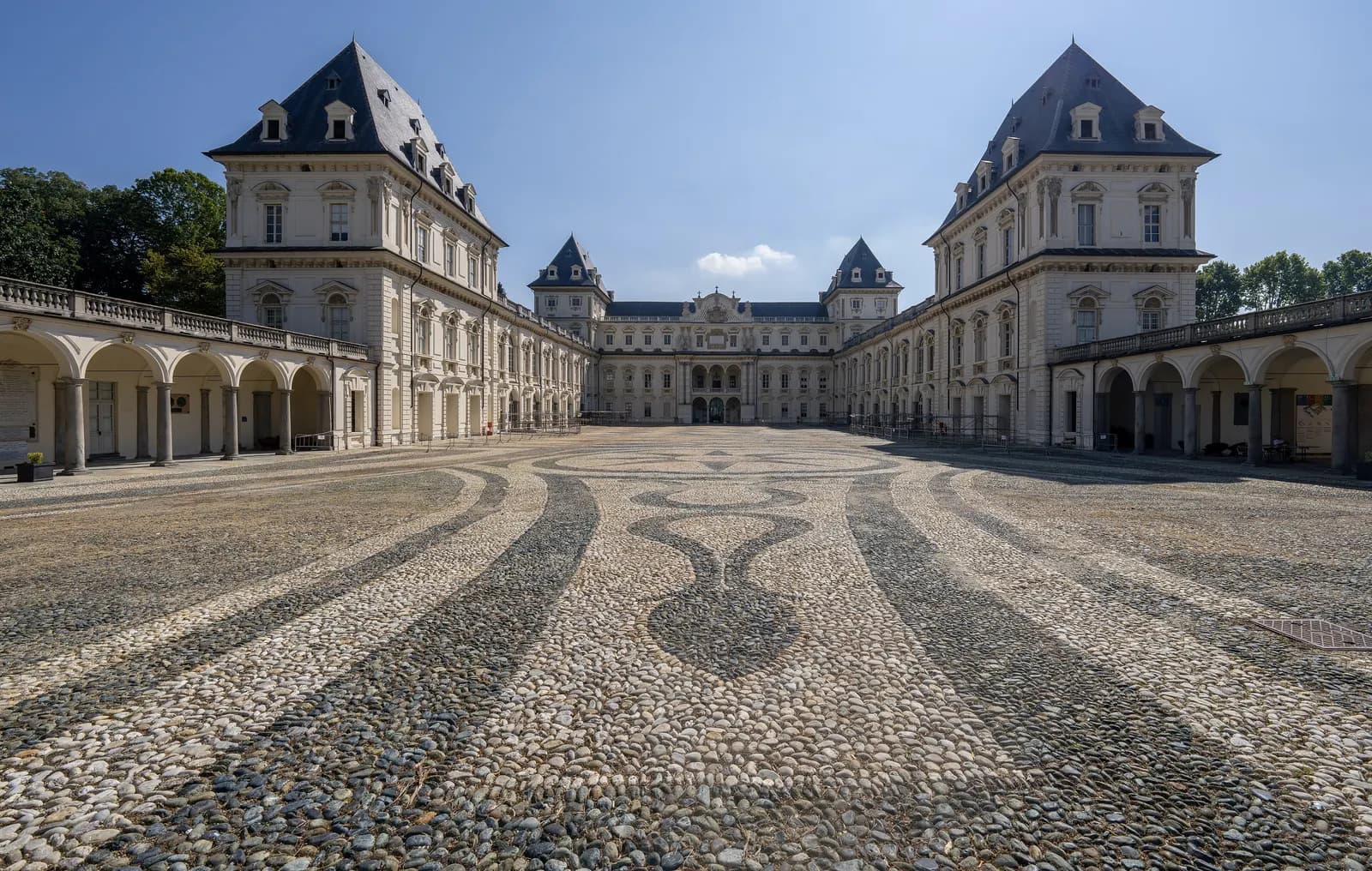 The courtyard of the Castello del Valentino in Turin, with its slate roofs, white pavilions, arcaded wings and a patterned cobble floor.
