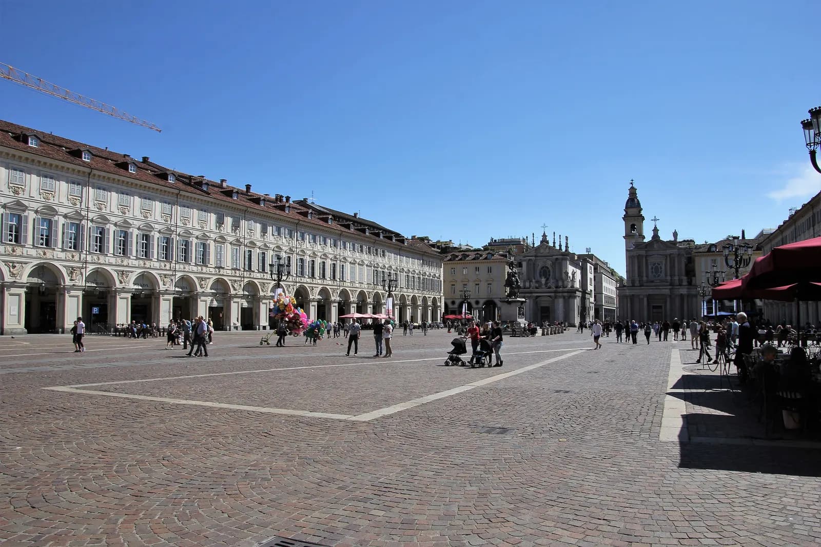 Piazza San Carlo in Turin on a clear day: long arcaded palace fronts, the twin church facades at the far end and people crossing the stone paving.