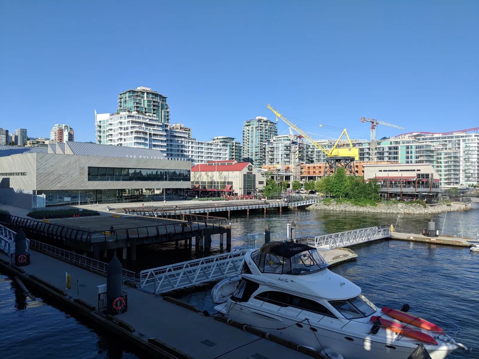 The Shipyards waterfront in North Vancouver seen from Lonsdale Quay, with the Polygon Gallery, a restored yellow crane, apartment blocks and a moored motor boat