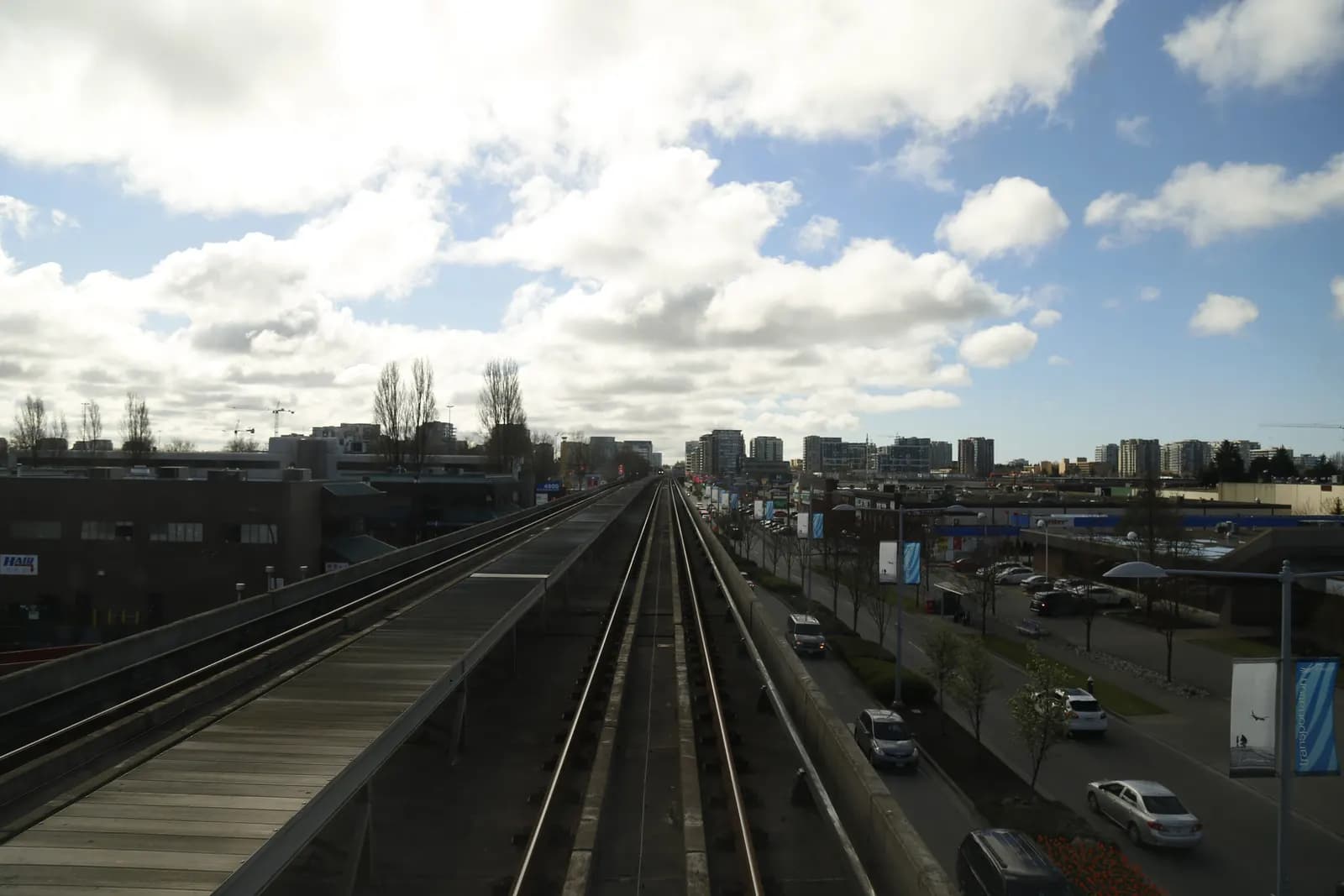 An elevated rail track running beside a road in Richmond, with cars below and apartment towers on the horizon