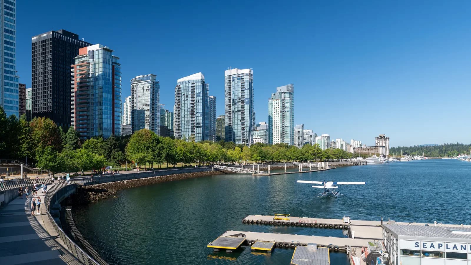 Glass apartment towers along Coal Harbour in Downtown Vancouver, with the seawall path, a floatplane on the water and the seaplane terminal dock