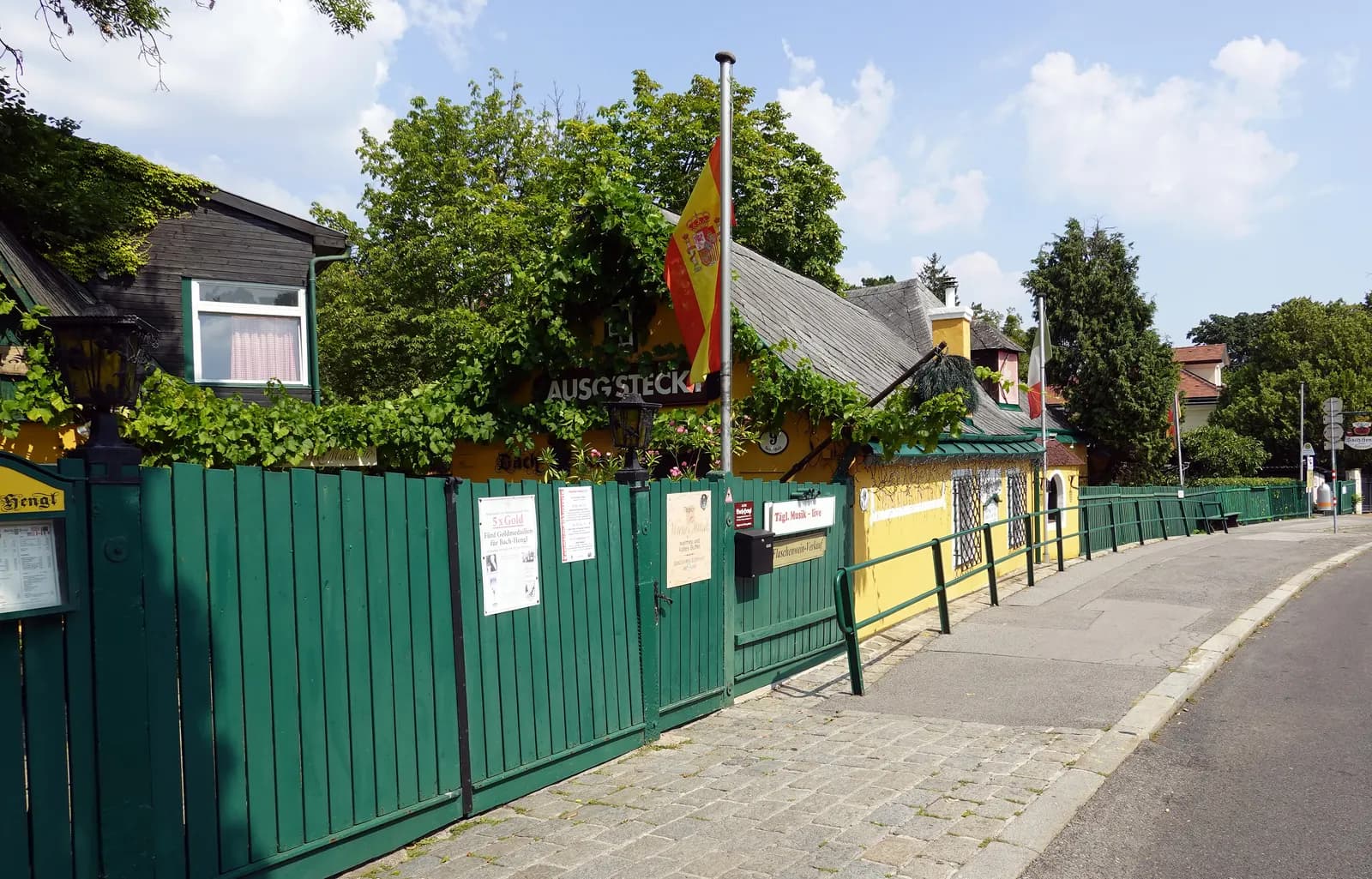 The Bach-Hengl wine tavern in Grinzing with a green wooden fence, vines over the house and an Ausg'steckt sign
