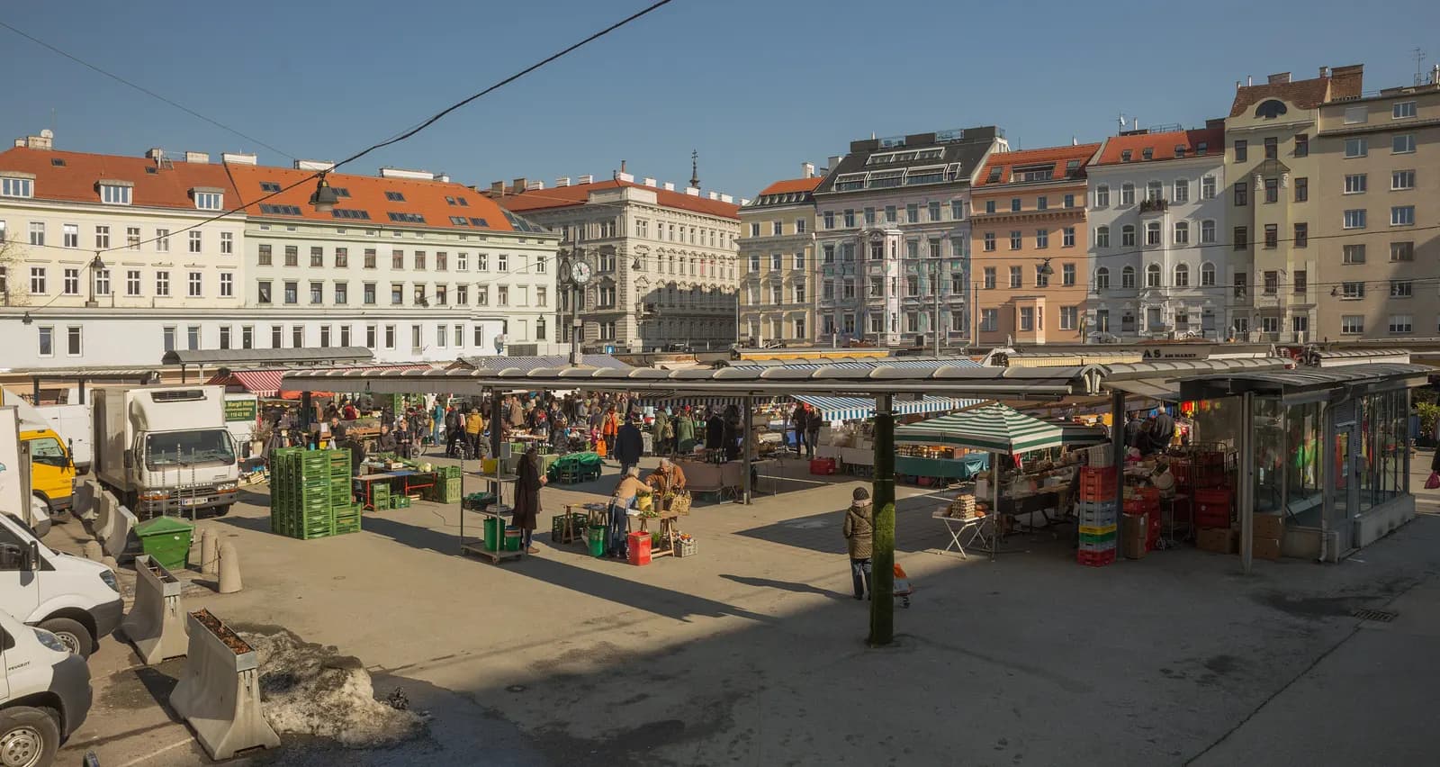 Stalls and shoppers at the Saturday farmers market on the Karmelitermarkt, with apartment houses around the square