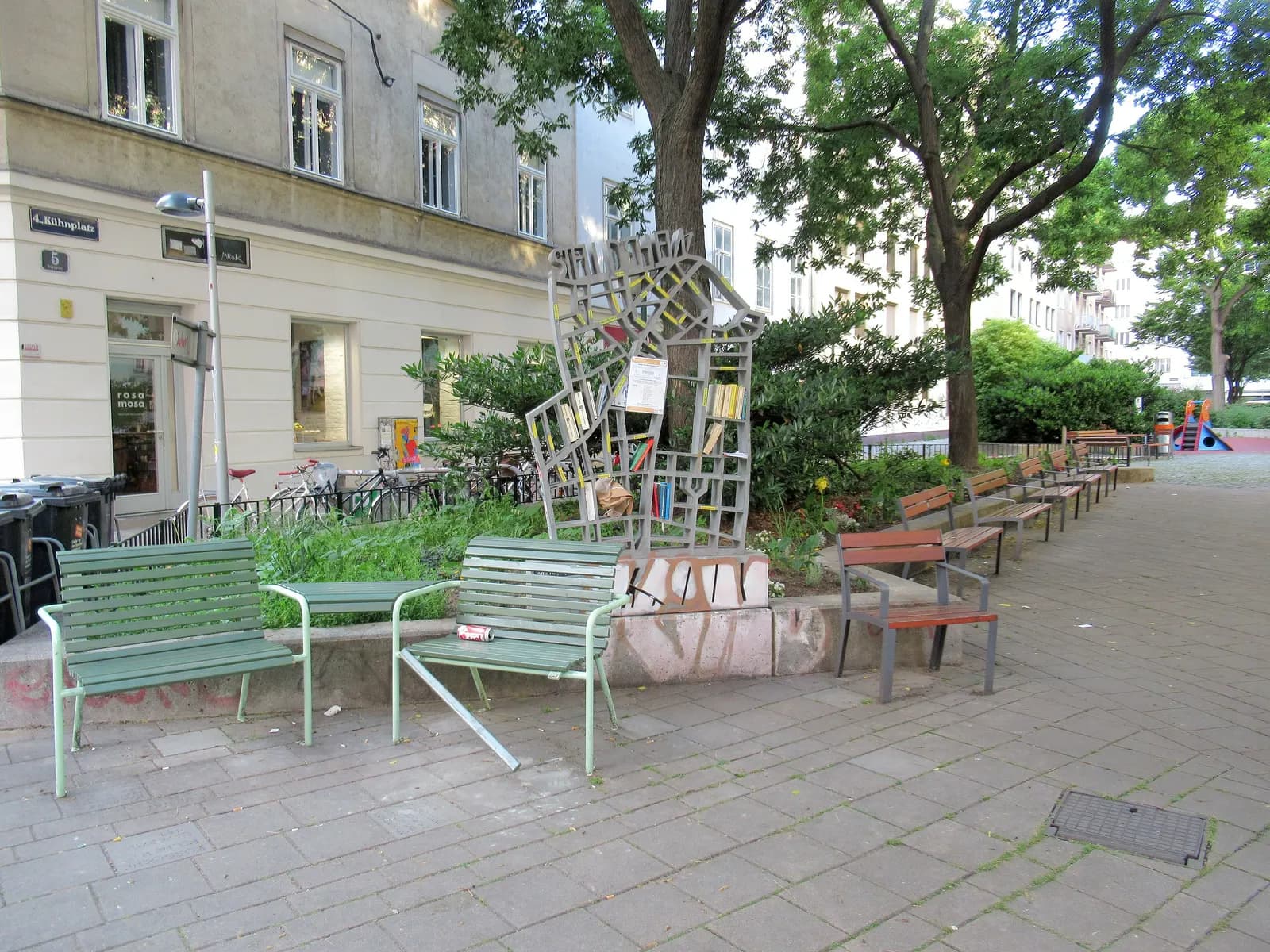 Kühnplatz in the fourth district, with an open public bookcase shaped as a sculpture, benches and trees in front of apartment houses