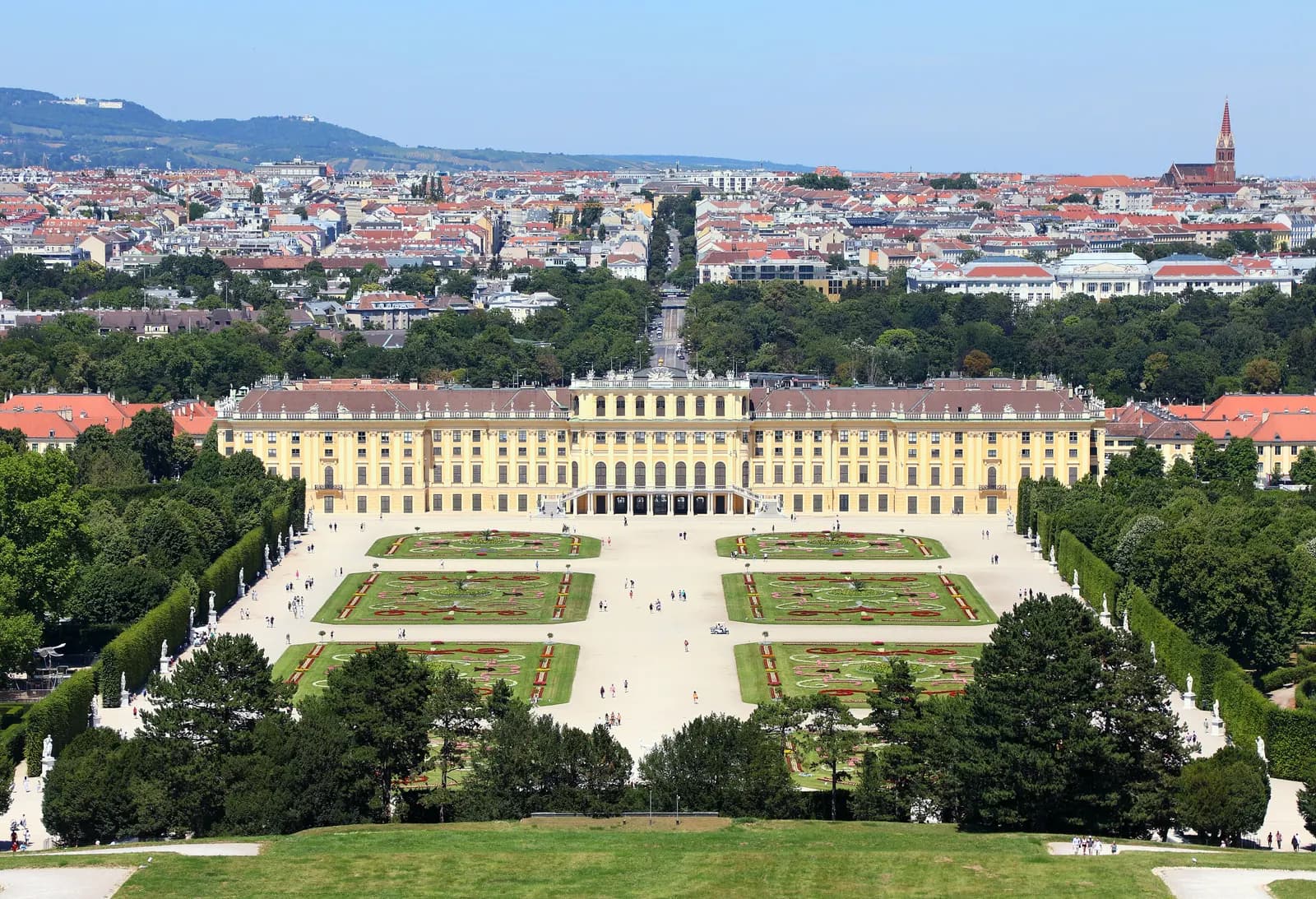 Schönbrunn Palace and its formal garden seen from the hill above the park, with the city and wooded hills beyond