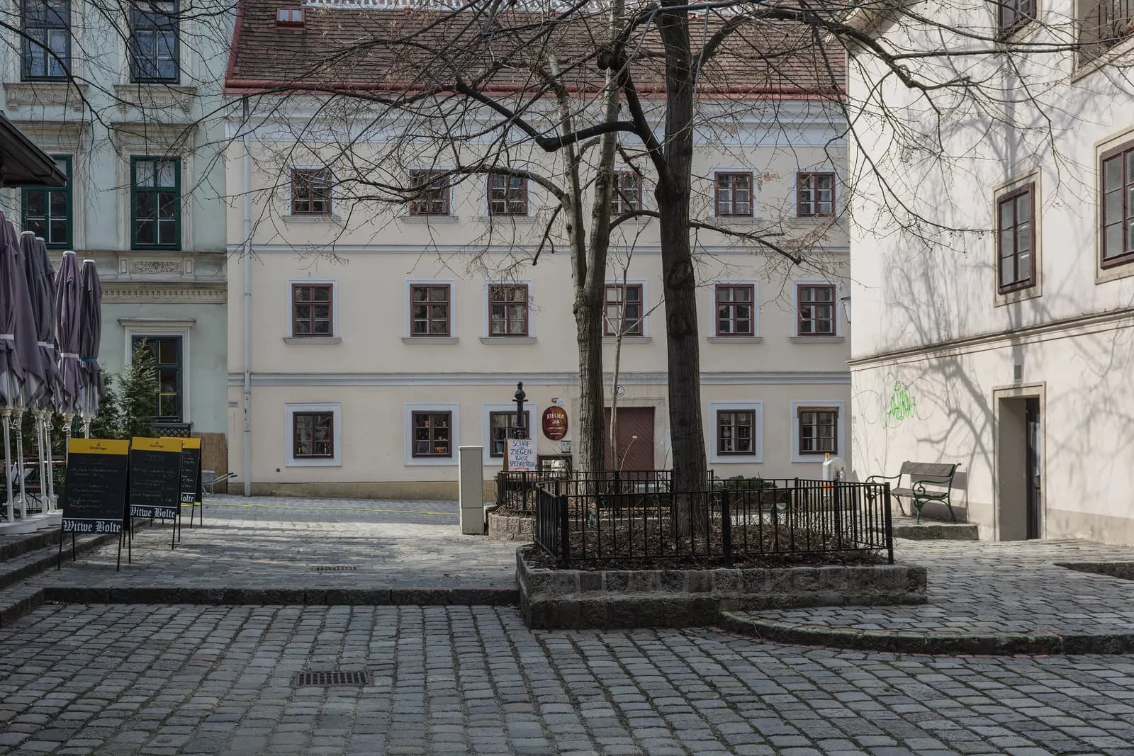 A small cobbled square off Spittelberggasse with a pale two-storey house, bare trees and a restaurant's menu boards