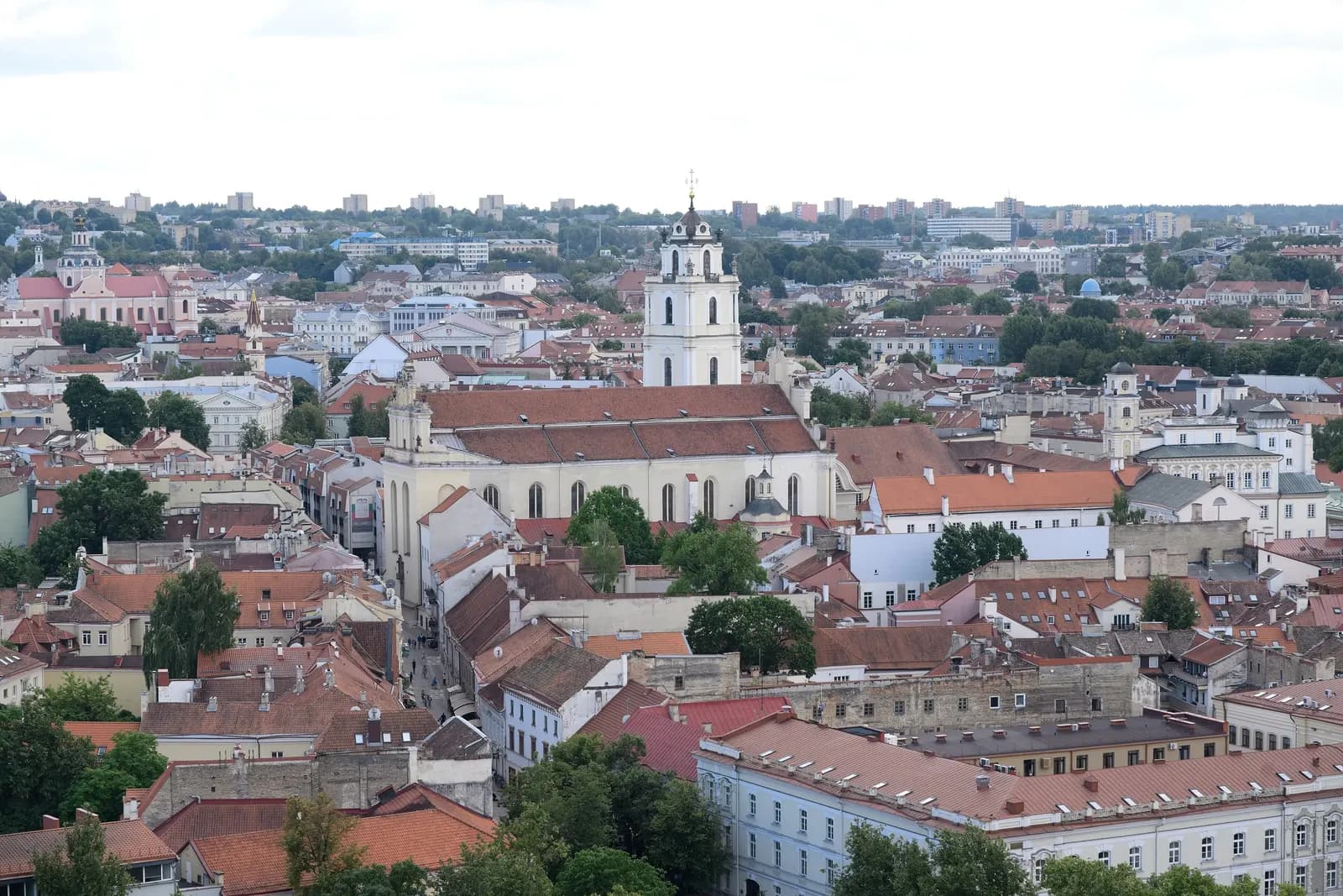 Vilnius Old Town from above: red-tiled roofs, a white bell tower and a church, with the newer city on the horizon