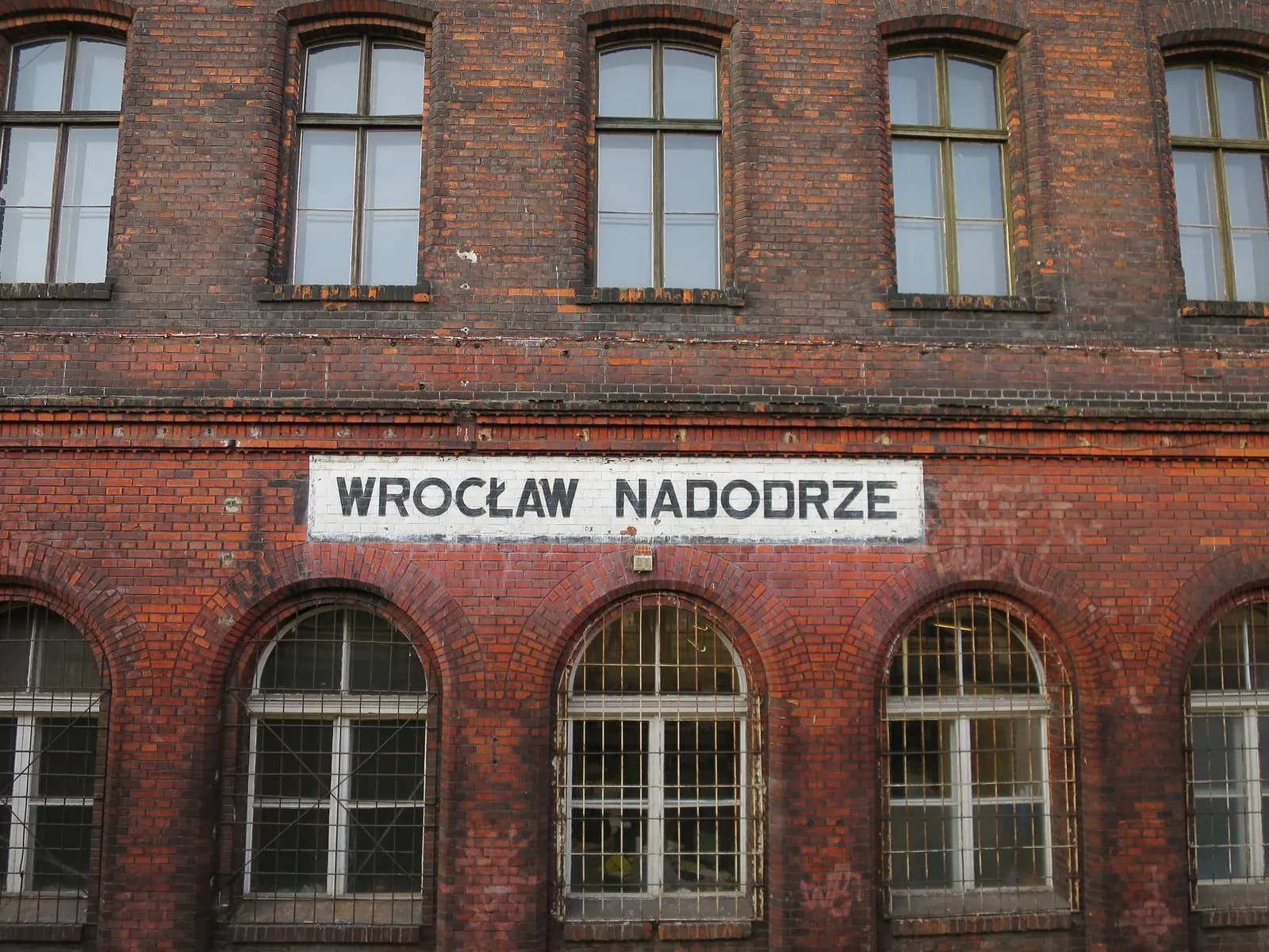 The red-brick facade of Wrocław Nadodrze railway station with its painted name sign and arched windows