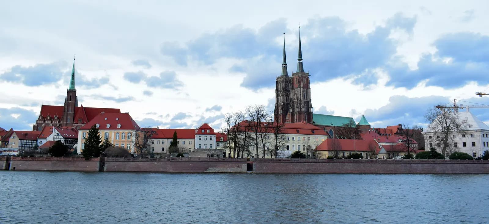 Ostrów Tumski seen across the Oder: the twin spires of Wrocław Cathedral and a brick church above red-roofed houses on the embankment