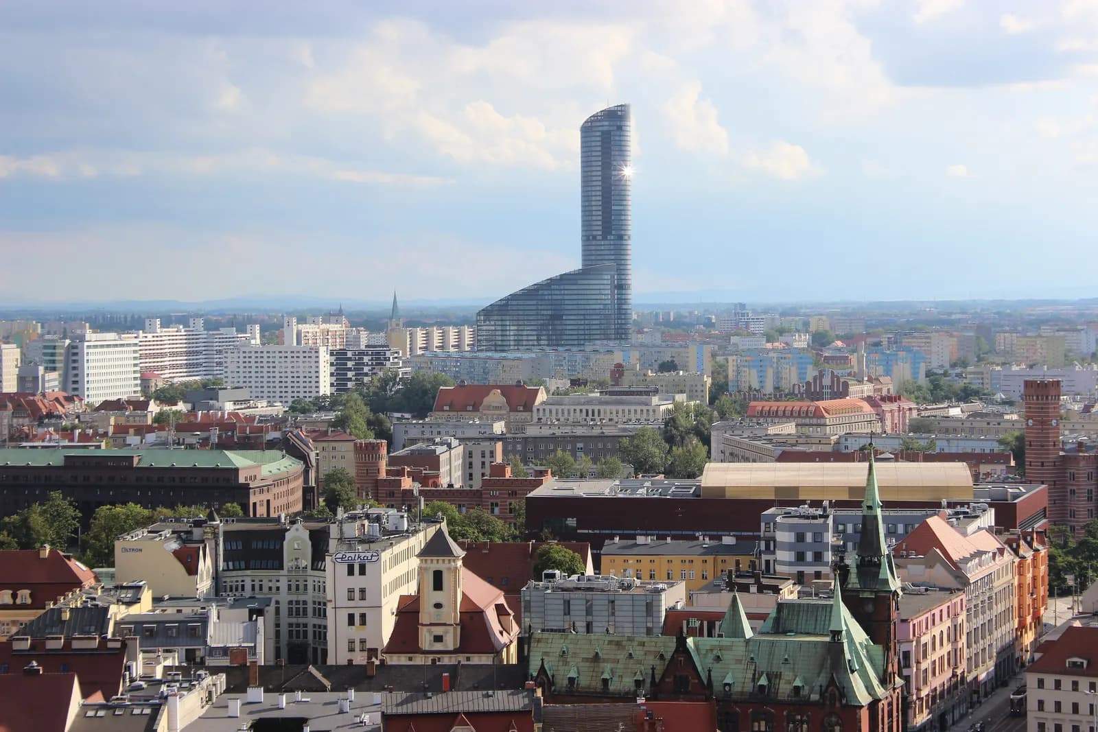 The Sky Tower rising above the rooftops of southern Wrocław, seen from a high viewpoint with green church spires in front