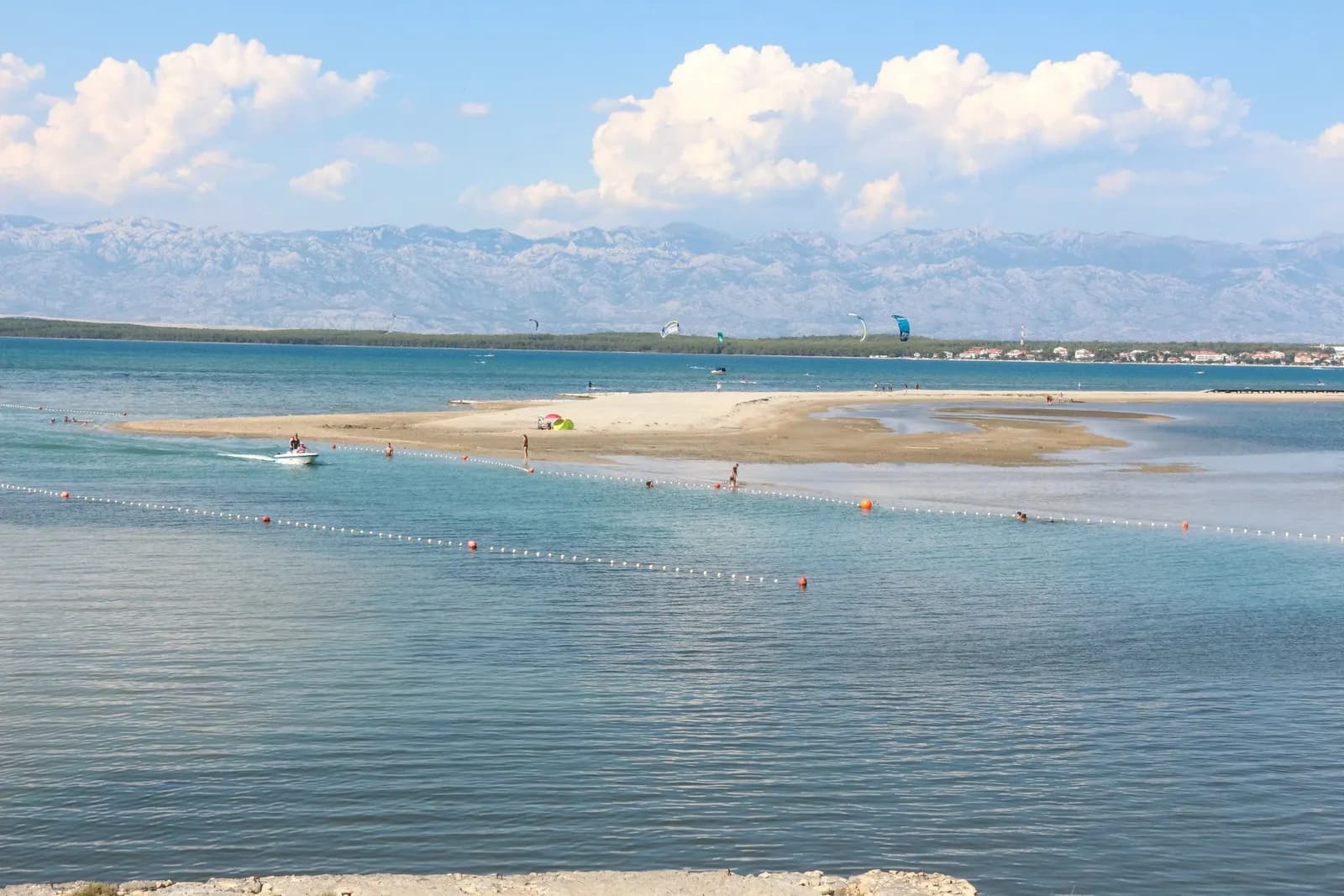 The long shallow sandbar of Queen's Beach at Nin, with swimmers, kitesurfers and the Velebit mountains across the water