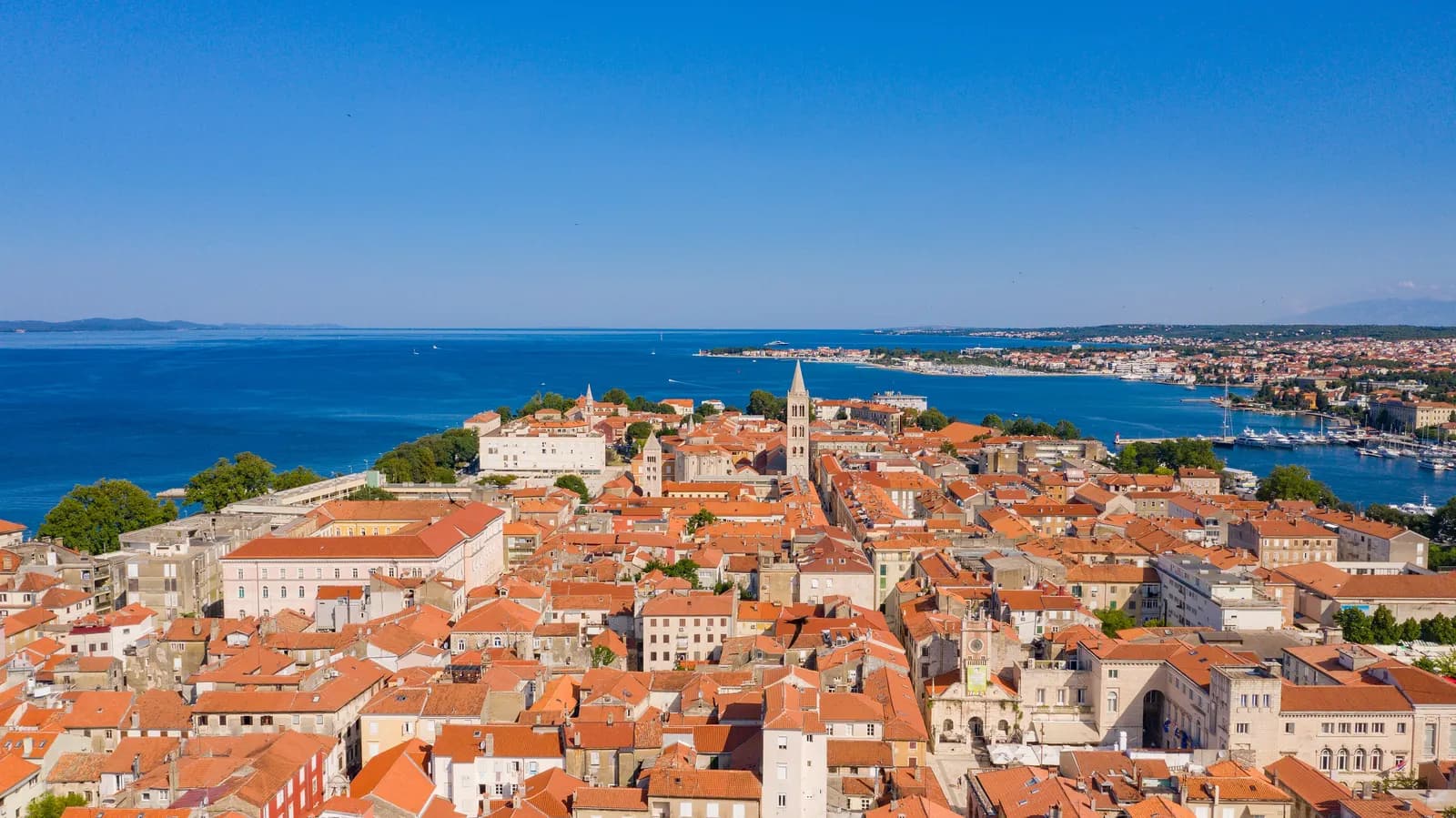 Red roofs of Zadar Old Town on its peninsula with the cathedral bell tower, the harbour on the right and the city's northern shore across the water