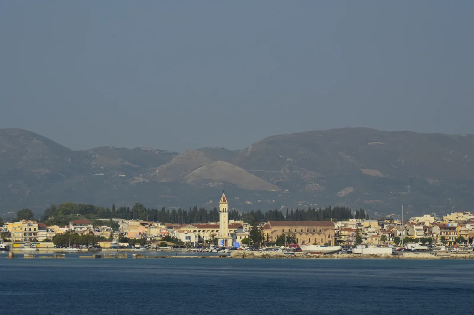The seafront of Zakynthos Town seen from the water, with the bell tower of the Agios Dionysios church and hills rising behind the houses