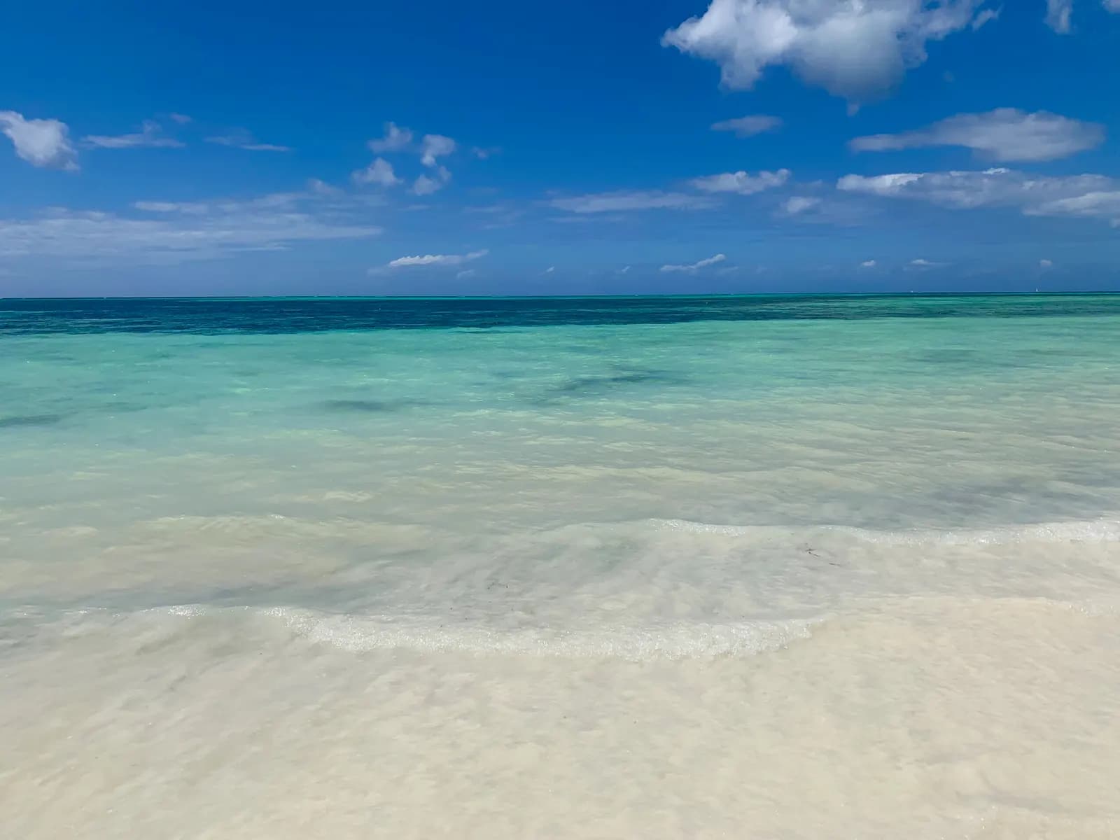 Clear shallow water over white sand at Kiwengwa beach on the north-east coast, under a blue sky with scattered clouds