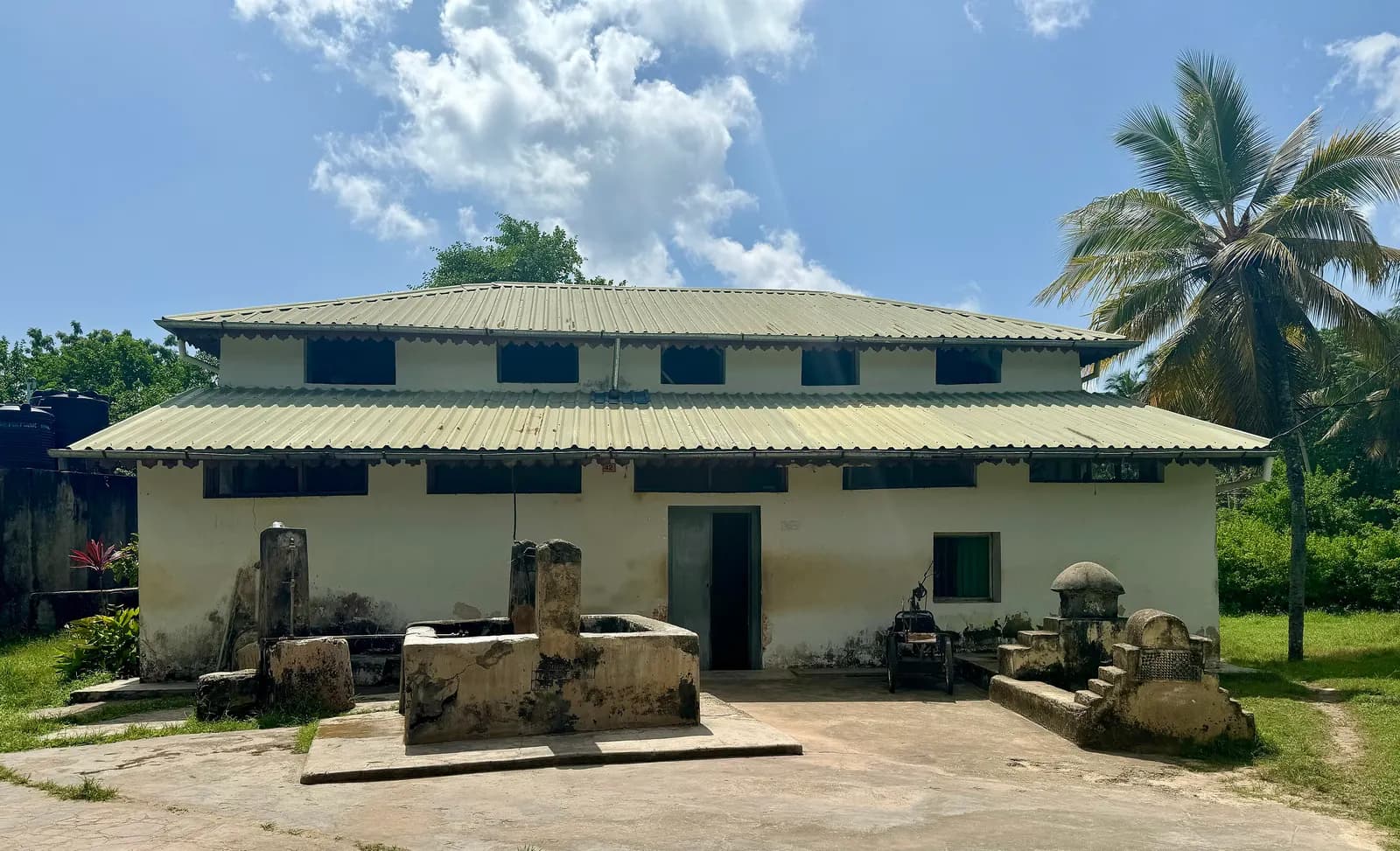 The historic Kizimkazi mosque at Dimbani, a white building with a green metal roof, with old tombs in front and palm trees at the side