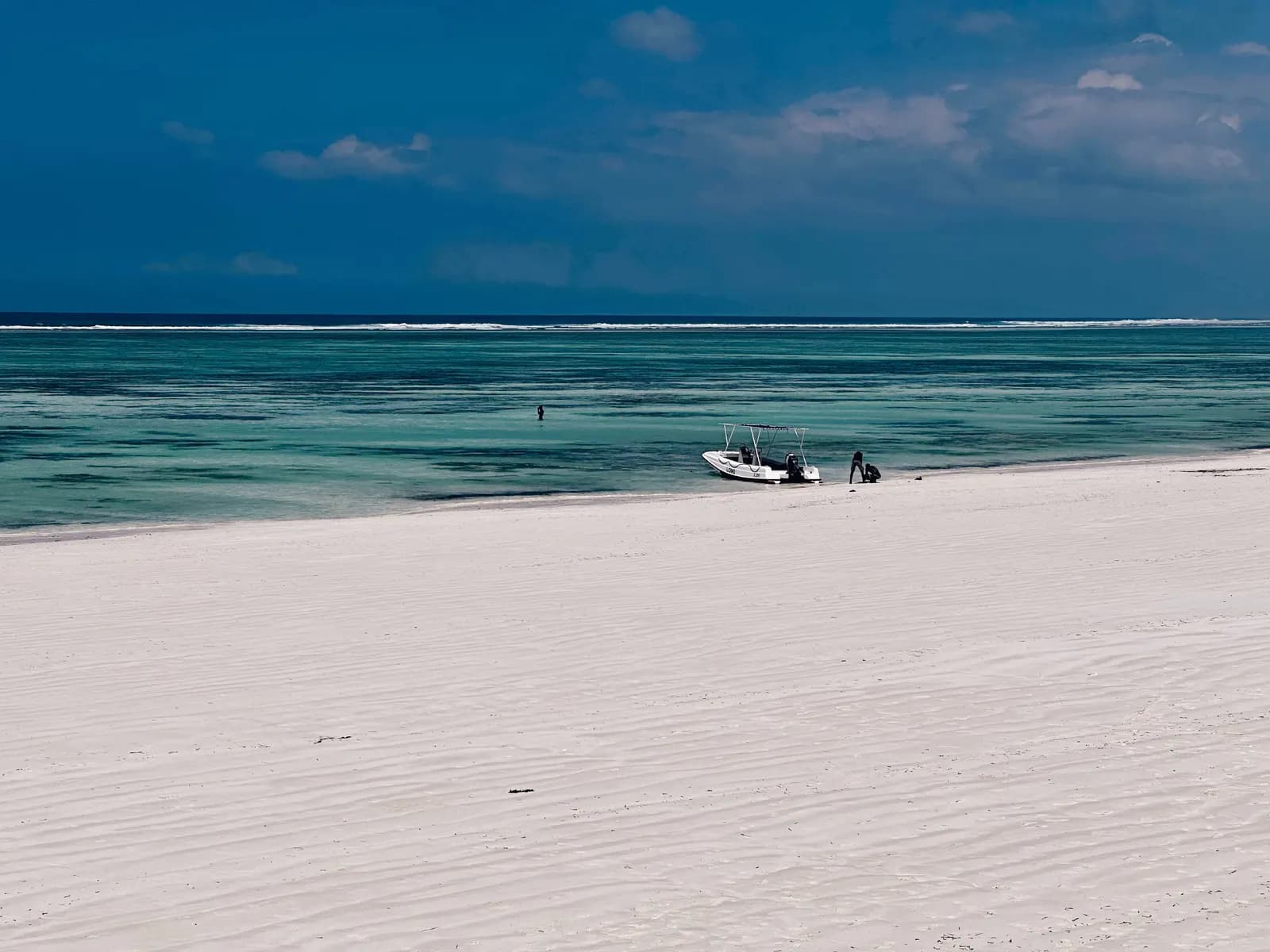 The wide white beach at Matemwe with a small motor boat at the water line, a turquoise lagoon and the reef on the horizon