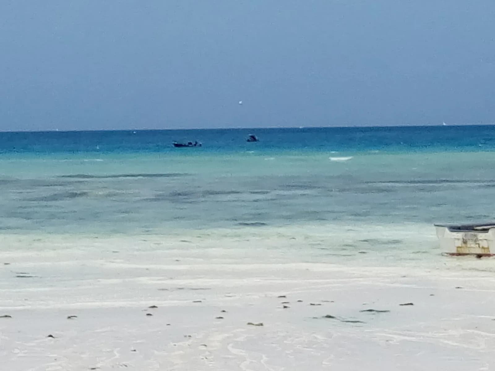 White sand and calm turquoise water at Nungwi beach, with two small boats out on the sea and a boat pulled up on the right